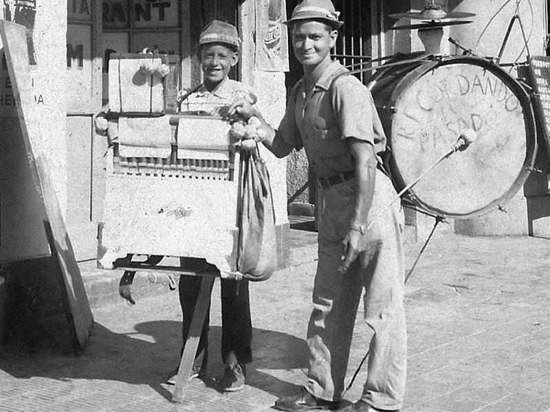 Organillero con su carro y un chinchinero en la calle, registro histórico